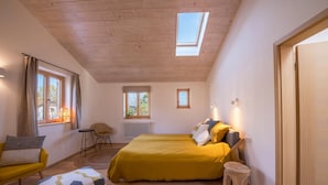 Un dormitorio con una cama, una silla, un taburete pequeño y una ventana con cortinas.