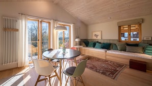 Una habitación amplia con techo de madera, una mesa de comedor con sillas, un sofá y un gran ventanal con cortinas.