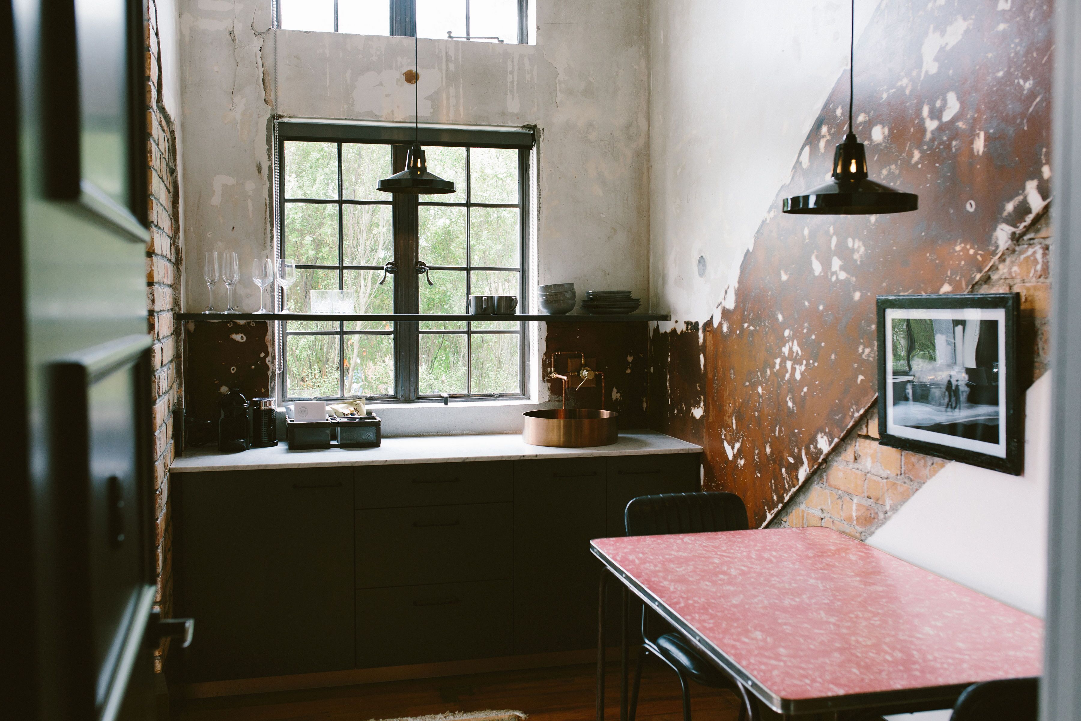 Une cuisine rustique avec une grande fenêtre, une table rouge et un luminaire suspendu.