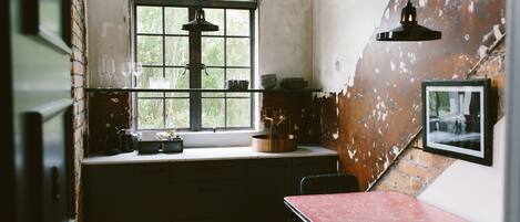 Una cocina rústica con un ventanal grande, una mesa roja y un colgador de lámpara.