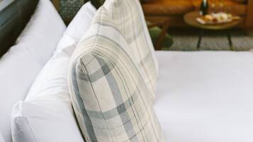 A neatly made bed with white and plaid pillows, a brown leather sofa, and a small round table with a bottle and glasses.