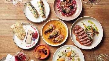 Variedad de platos sobre una mesa de madera, incluyendo mariscos, carne y verduras, con copas de vino y cubiertos.