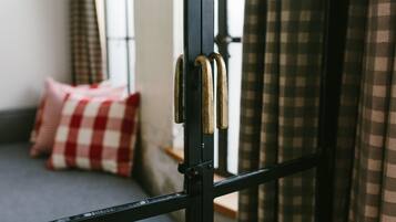 Una habitación con un cojín a cuadros, una ventana con cortinas y una reja de metal.