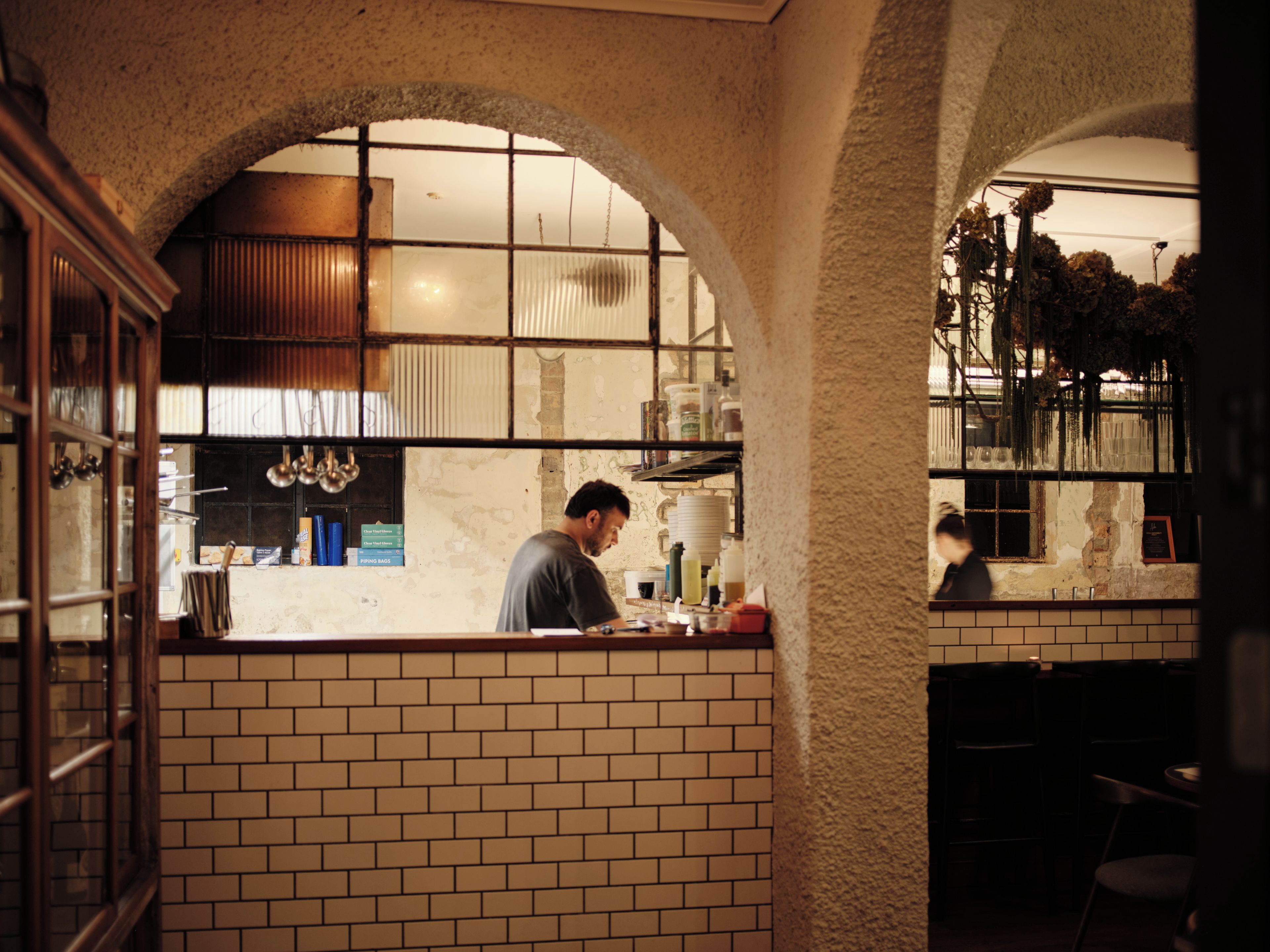 L’intérieur d’un restaurant avec des murs en briques, des fenêtres en arc de cercle et un espace bar.