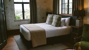 Un dormitorio con cama, mesita de noche, una silla y vistas por la ventana.