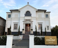 A two-story building with a white facade, a central entrance with a dark door, and a cross on top.