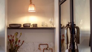 Una cocina con un lavamanos de cobre, una lámpara colgante y una repisa con platos y tazones.