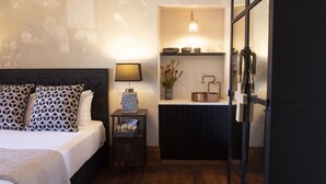 Un dormitorio con cama, mesita de noche, lámpara y una pequeña kitchenette con fregadero y encimera.