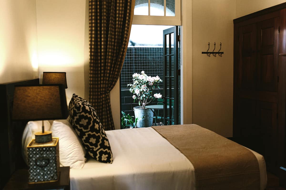 A neatly made bed with a patterned pillow, a bedside lamp, and a vase with flowers.