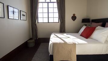 A bedroom with a large bed, a window with curtains, a wall-mounted lamp, and framed pictures.