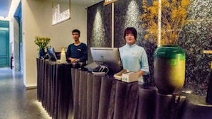 Una recepción con dos personas, una computadora portátil, un florero y una planta pequeña.