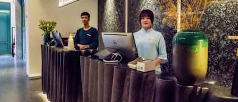 A reception desk with two individuals, a laptop, a vase, and a small plant.