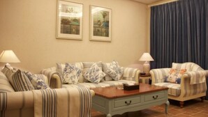 A living room with striped sofas, a coffee table, and two lamps. - Victoria Hotel Huizhou (Huizhou)