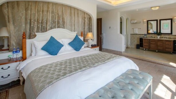 A spacious bedroom with a large bed, a sitting area, and a view of the bathroom. - Victoria Hotel Huizhou (Huizhou)