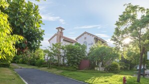 A building with a white facade and a red roof, surrounded by lush greenery and a paved driveway. - Victoria Hotel Huizhou (Huizhou)