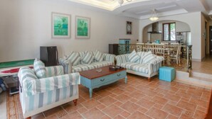 A living room with striped sofas, a coffee table, and a television. There is a kitchen area in the background with a dining table and chairs. - Victoria Hotel Huizhou (Huizhou)