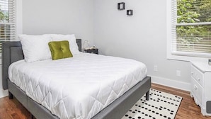 A bedroom with a bed, a nightstand, a dresser, and a window with blinds. - Cool City Cottage (MINS FROM AIRPORT/CITY) 2B 1B (Stone Mountain)