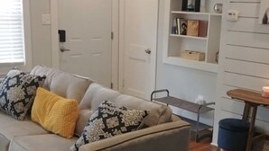 A living room with a sofa, a small table, and a bookshelf. - Cool City Cottage (MINS FROM AIRPORT/CITY) 2B 1B (Stone Mountain)