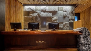 Un mostrador de recepción con tres monitores, un fondo de pared de piedra y un techo de madera.