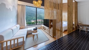 Una habitación de hotel moderna con un ventanal grande, un sofá, una mesita, un televisor y una cama.