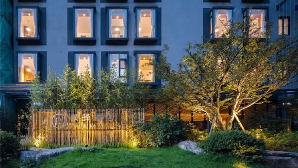 Un edificio con varias ventanas, un jardín cuidado con un árbol y una cerca de bambú.