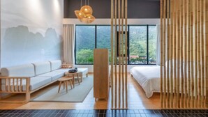 Una habitación de hotel moderna con sofá, cama, un separador de madera y vistas a zonas verdes.