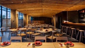 Un restaurante espacioso con varias mesas y sillas, techo de madera y grandes ventanales con vistas al exterior.