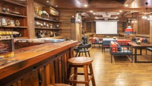 Un espace bar accueillant, doté de meubles en bois, d’un écran de projection et de différents types de sièges.