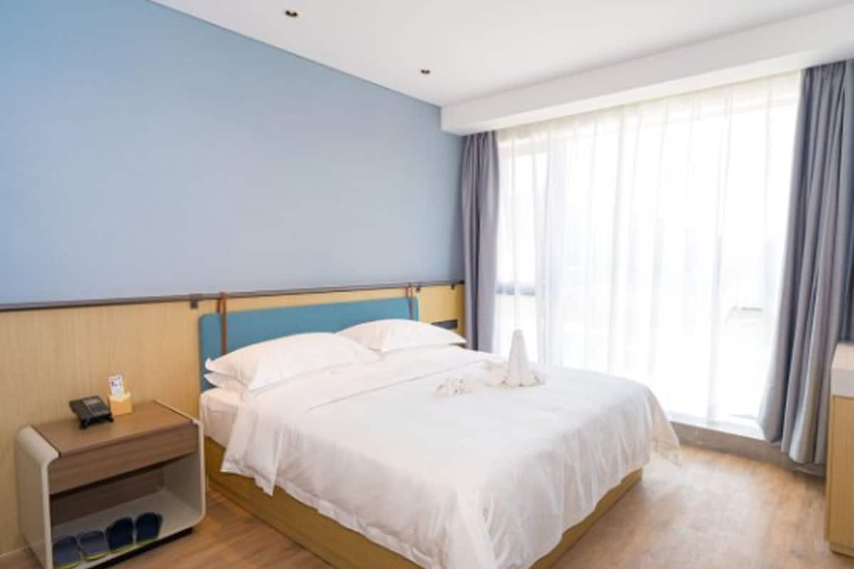 A hotel room with a bed, a nightstand, a shoe rack, and a window with curtains.