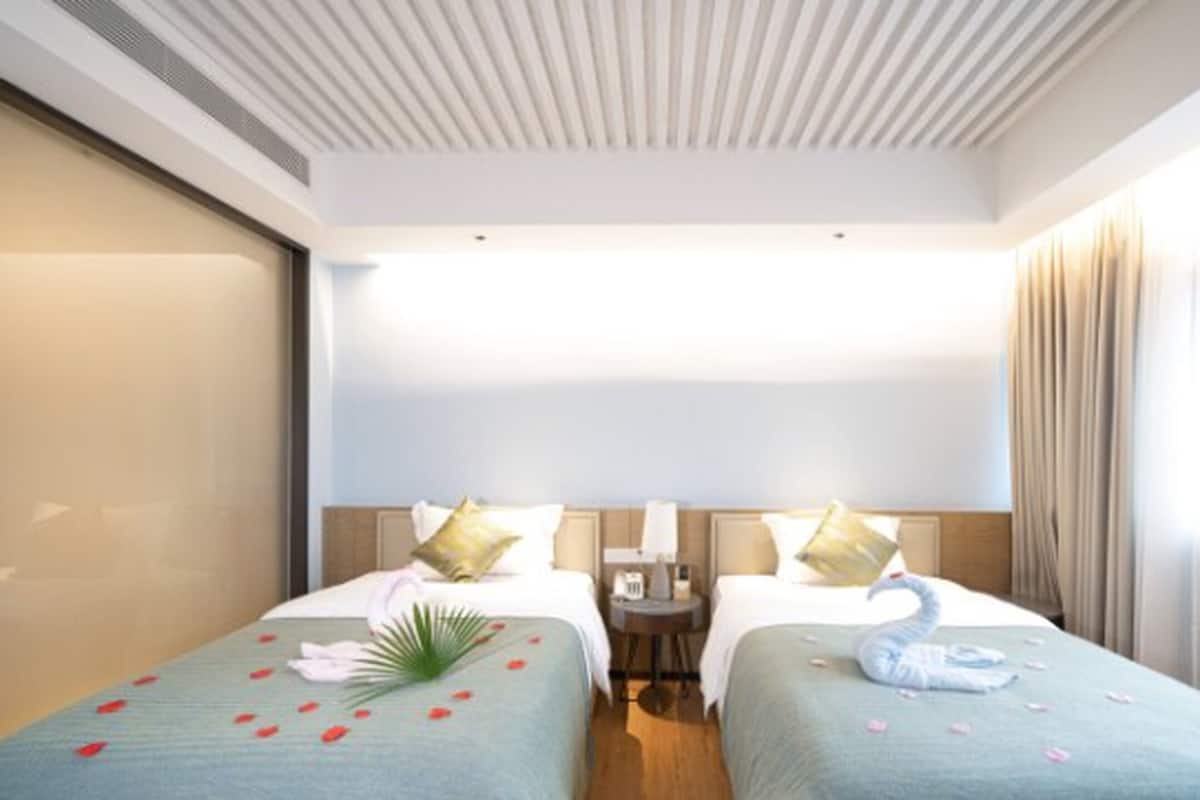 A hotel room with two beds, a nightstand, a lamp, and a large window with curtains.