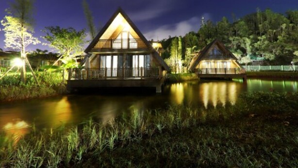Deux cabanes en bois dotées de balcons, entourées d’un lac et d’arbres, de nuit.