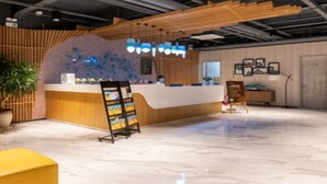Un espace d’accueil comprenant un comptoir en bois, une plante en pot et un coin salon avec des chaises jaunes.