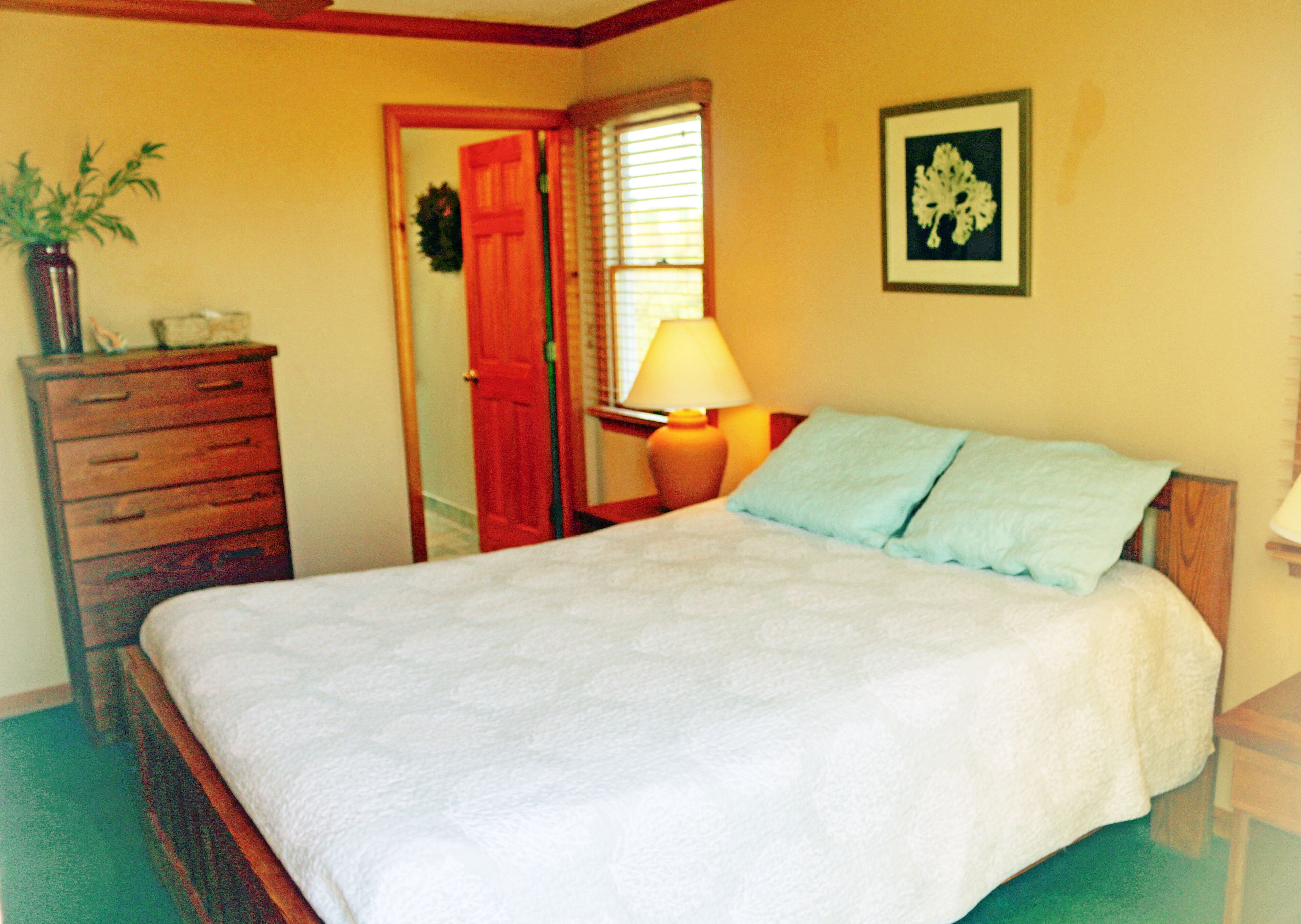 A bedroom with a bed, dresser, lamp, and a framed picture on the wall.