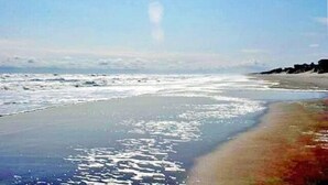 A beach with waves approaching the shore, a clear sky, and a rocky coastline. - WH852- Stunning! Private Pool, Hot Tub, 4 BRs, Pool Table and Screened Porch! (Corolla)