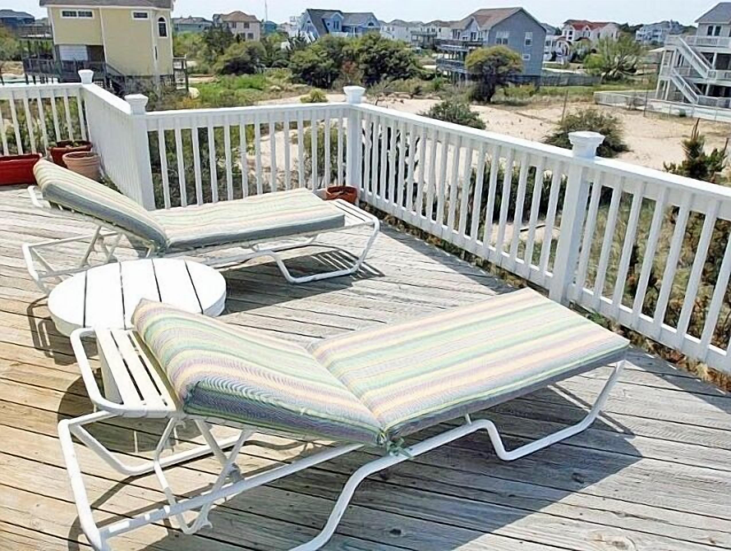 Een houten terras met twee loungesteunen en een tafel, omringd door een witte hekwerk.