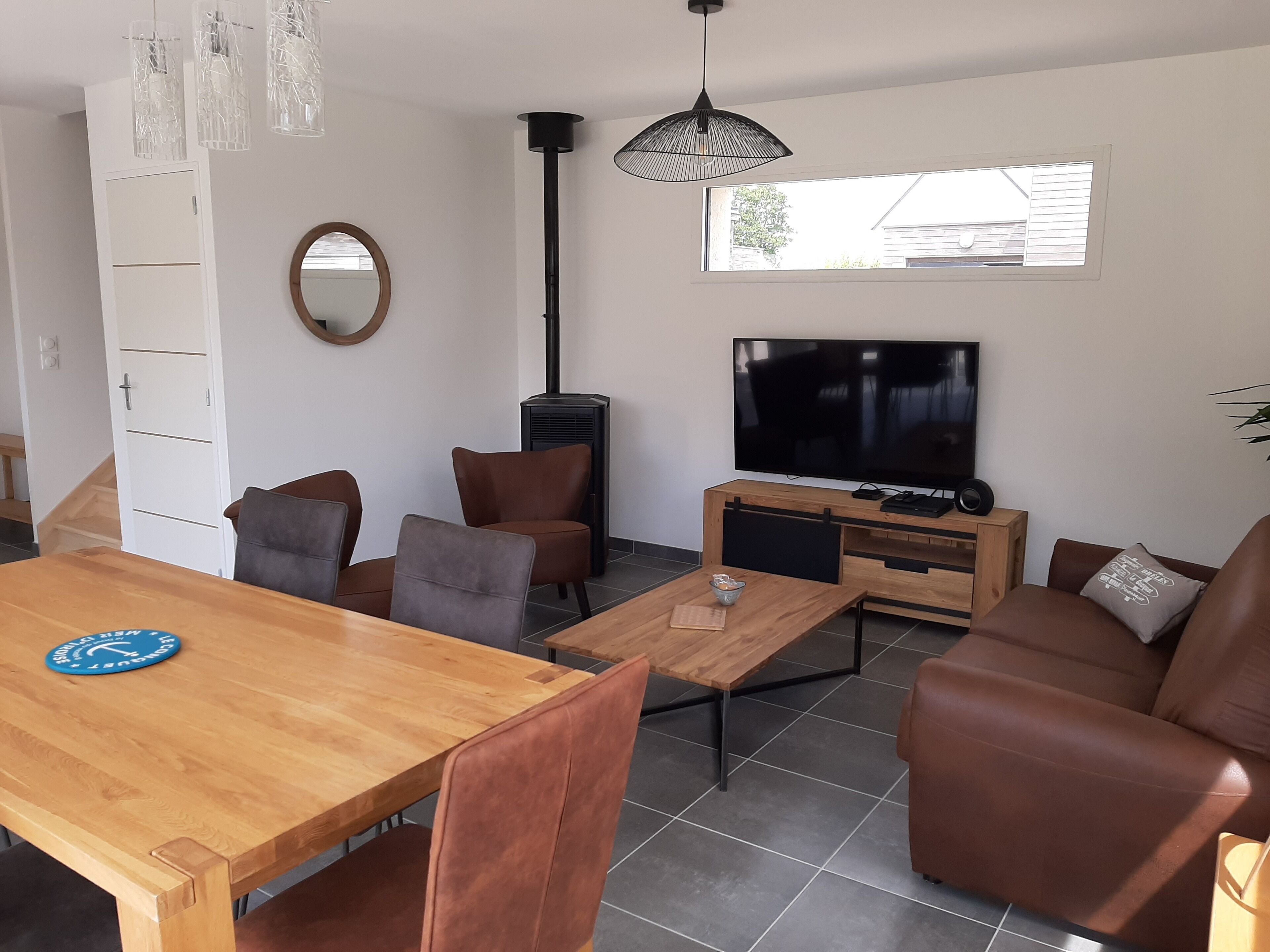 Un salon moderne avec une table à manger en bois, un canapé en cuir marron et un téléviseur à écran plat.
