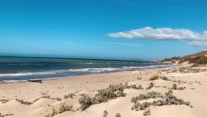 Una playa con dunas de arena, un bote y una torre a lo lejos.