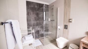 Un baño moderno con ducha envuelta en vidrio, inodoro y toallero con toallas dobladas.