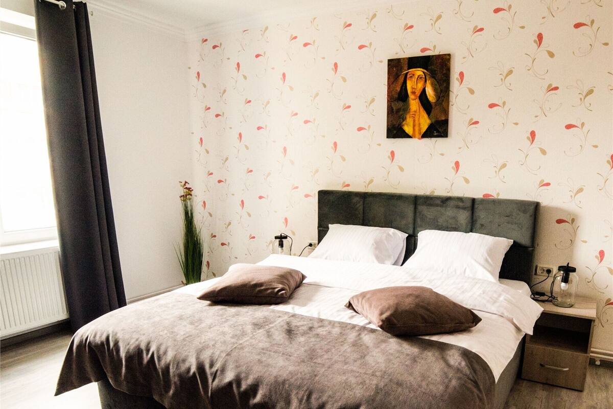 A neatly made bed with a striped rug, a nightstand with a lamp, and a wall with a floral pattern.