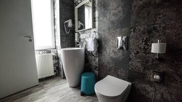 A bathroom with a large sink, a toilet, a blue trash bin, and a mirror.