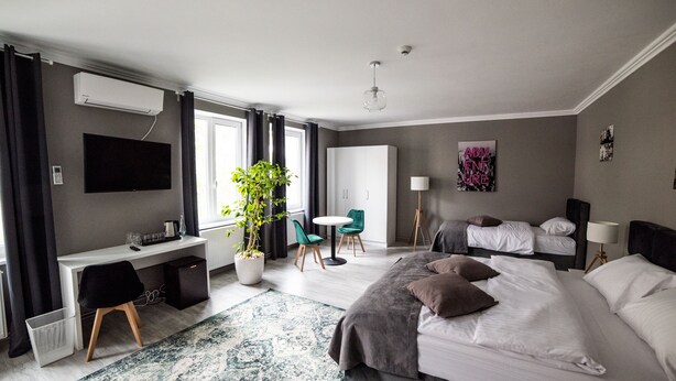A modern hotel room with a large bed, a desk, a chair, a potted plant, and a television.