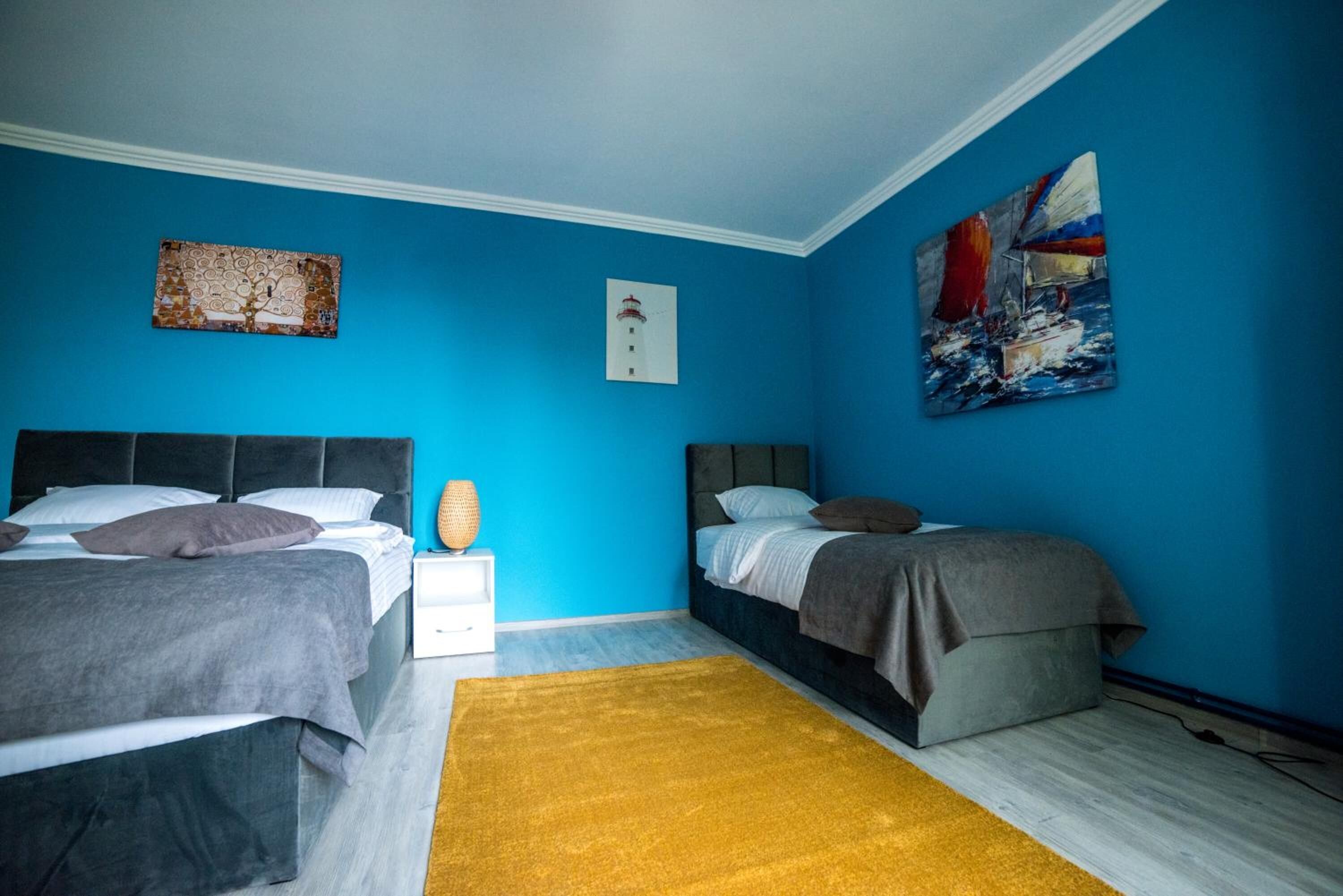 A bedroom with two beds, a yellow rug, and artwork on the walls.