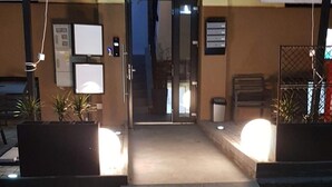 A hotel entrance with a ramp leading to the door, a security desk, and a sign indicating the check-in area.
