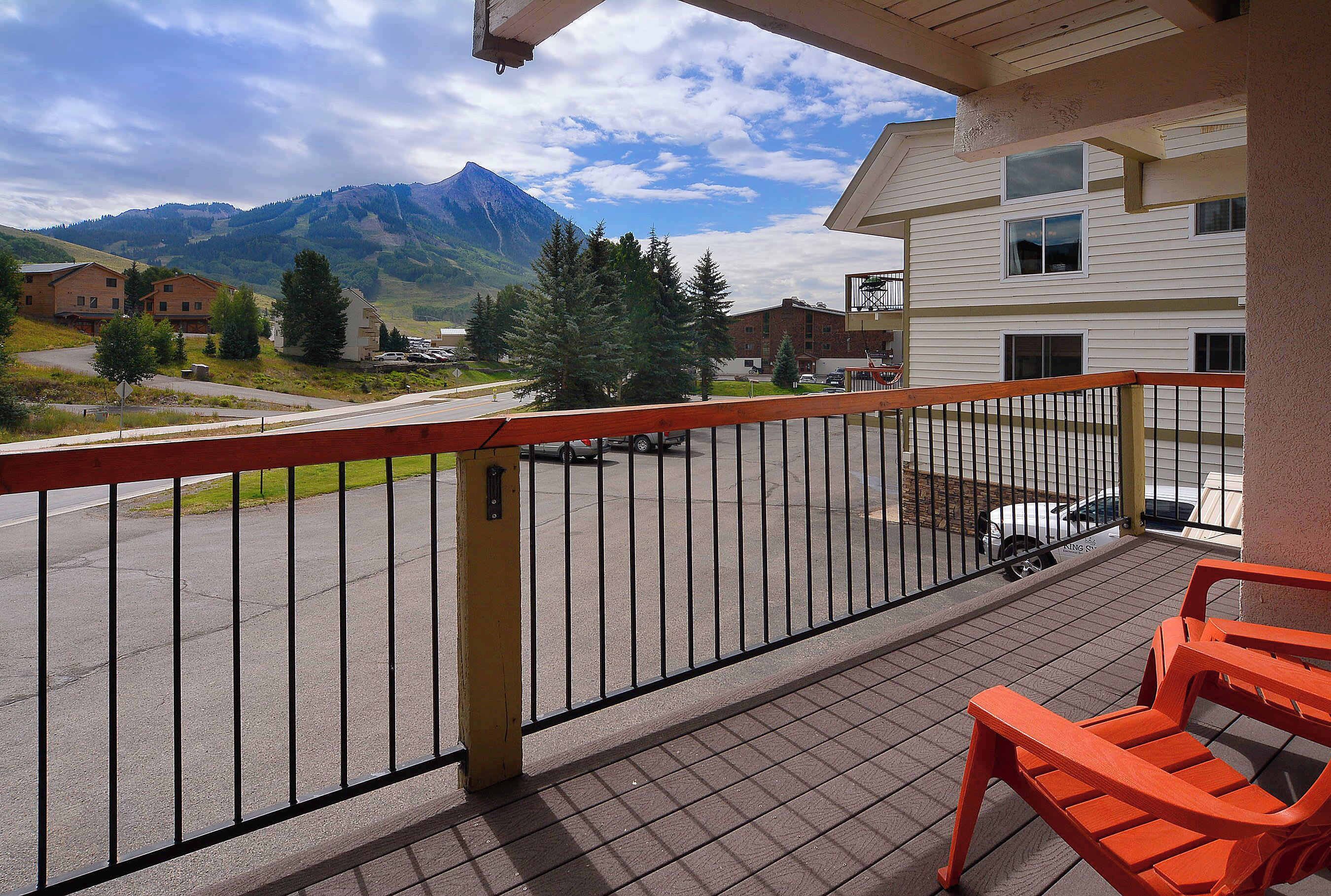 A balcony with a view of a mountain, a parking area, and a building with multiple windows.