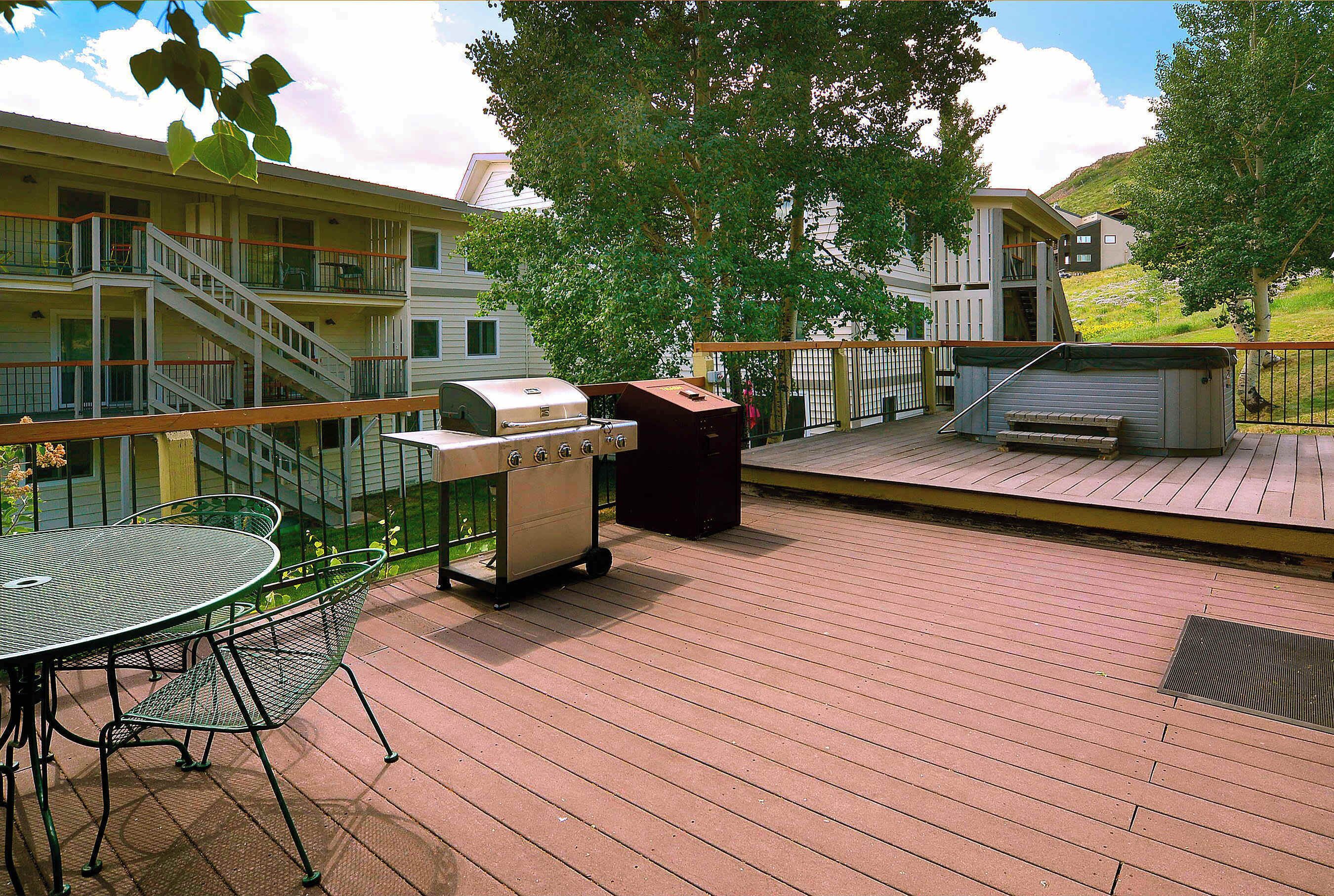 A deck with a grill, a table with chairs, and a view of a building with multiple balconies.