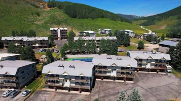 A multi-story hotel with a parking lot, surrounded by green hills and mountains.