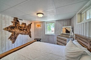 Une chambre avec une grande moquette en fourrure, un lit avec une literie blanche, une tête de lit en bois, une table de chevet, une commode et une fenêtre donnant sur un paysage verdoyant.