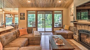 A spacious living room with a fireplace, leather sofas, and a dining area with a large window overlooking a deck. - Bigfork Modern Living - Pet & Family Friendly! (Bigfork)