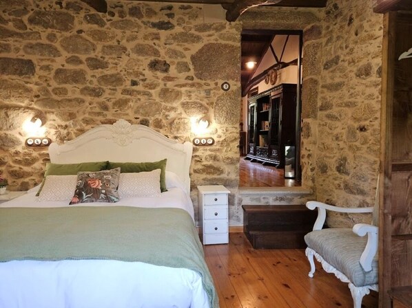 Ein Schlafzimmer mit Steinwand, einem Bett mit weißem Kopfteil, Nachttischen, einem Stuhl und einem Spiegel.