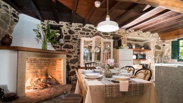 A rustic dining area with a stone fireplace, wooden beams, and a table set for a meal. - A Casa dos Avós - House with swimming pool, barbecue in the middle of nature in A Coruña. (Oza de los Ríos)